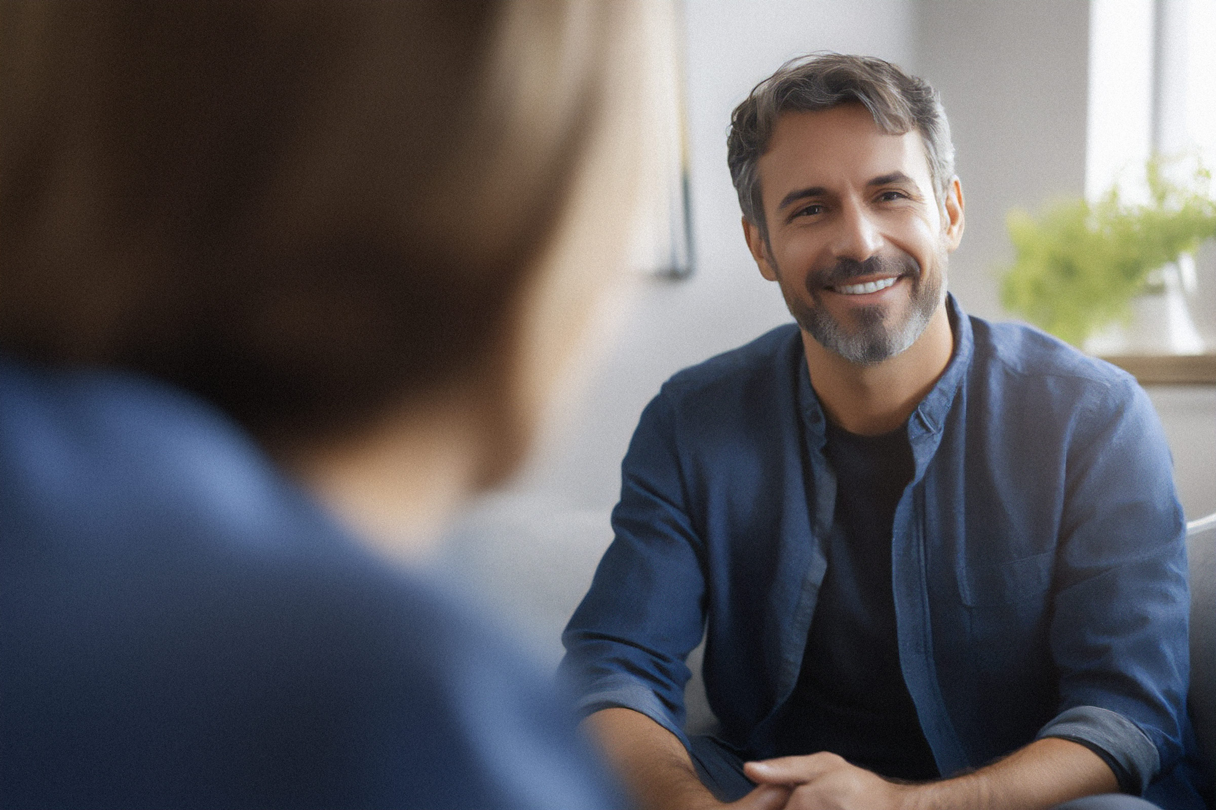Ein freundlich lächelnder Mann mit positiver Ausstrahlung, der einer Patientin zuhört. Er ist Diplom-Psychologe.